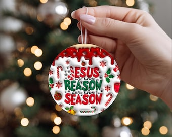 May include: A round Christmas ornament with the text "Jesus is the Reason for the Season." The ornament has a red and white design with candy canes, snowflakes, and holly. It is held by a person in front of a Christmas tree.