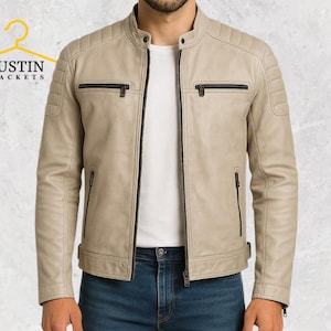 Puede incluir: Chaqueta de cuero de color beige claro con cuello alzado y detalles acolchados en los hombros. La chaqueta tiene múltiples bolsillos con cremallera y cierre frontal con cremallera. La marca "JUSTIN JACKETS" es visible en la esquina superior izquierda.