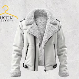 Puede incluir: Chaqueta de cuero sintético blanco con cuello y forro de borreguito. La chaqueta tiene cierre de cremallera, dos bolsillos delanteros y cinturón con hebilla en la cintura. La marca "JUSTIN JACKETS" está en la esquina superior izquierda.
