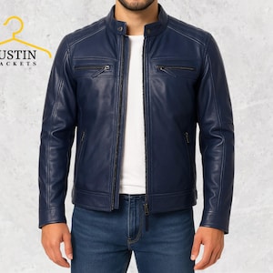 Puede incluir: Chaqueta de cuero azul marino con cuello alzado y bolsillos con cremallera. La chaqueta tiene cierre de cremallera frontal y se usa con vaqueros azules. El logotipo "JUSTIN JACKETS" es visible en la esquina superior izquierda.