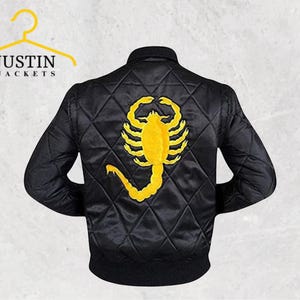 May include: Black bomber jacket featuring a yellow scorpion emblem on the back. The jacket has a diamond-quilted pattern and a ribbed collar and cuffs. The text "JUSTIN JACKETS" is above the jacket.