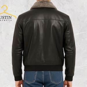 Puede incluir: Chaqueta de cuero negro con cuello de borrego y dobladillo acanalado. La chaqueta tiene un estilo bomber cl&aacute;sico con cremallera y un logotipo en la percha. El modelo lleva vaqueros azules.