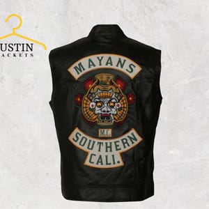 Op de afbeelding: Zwarte leren vest met een groot geborduurd embleem met de tekst "MAYANS" en "SOUTHERN CALI." Het embleem bevat een gedetailleerde afbeelding van een gestileerd gezicht met een hoofdtooi. Het vest heeft een klassieke biker-stijl.