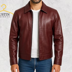 May include: A burgundy leather jacket with a collared neckline and a front zipper closure. The jacket has long sleeves and a tailored fit. The brand name "JUSTIN JACKETS" is displayed on a yellow hanger in the upper left corner.