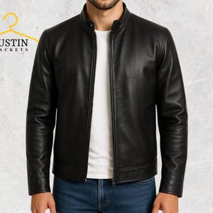 Op de afbeelding: Zwarte leren jas met een opstaande kraag en een ritssluiting aan de voorkant. De jas heeft lange mouwen en een getailleerde pasvorm. De merknaam "JUSTIN JACKETS" staat op een gele hanger. Het model draagt een wit t-shirt en een blauwe jeans.