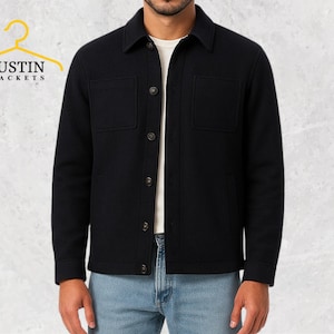 May include: Black jacket with two front pockets and button closures. The jacket has a collared neckline and is worn over a white shirt and blue jeans. The brand name "JUSTIN JACKETS" is visible on a yellow hanger.