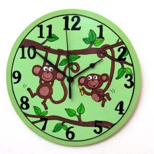 May include: A green round clock with two monkeys hanging from branches. The clock face has black numbers and hands. One monkey is holding a banana.