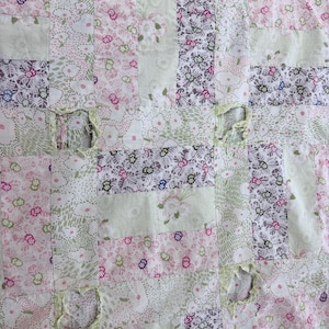 May include: A patchwork quilt with a variety of floral patterns in pink, green, and white. The quilt is made of rectangular fabric pieces sewn together. Some areas show wear and tear with visible holes.