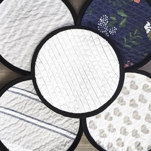 May include: Five round, black-rimmed pot holders with different patterns. The patterns include a white and gray striped pattern, a white and gray heart pattern, a white and gray striped pattern, a white and gray striped pattern, and a blue and white floral pattern.