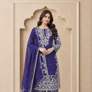 May include: A deep blue three-piece outfit consisting of a long-sleeved tunic, wide-leg trousers, and a sheer dupatta. The tunic features intricate silver and light blue embroidery around the neckline and hem. The text EV ETHNIC VILLA is visible.