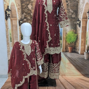 May include: A matching set of two maroon outfits featuring long-sleeved tunics and wide-leg trousers. Both garments are adorned with intricate gold embroidery, sequins, and scattered pearl-like beads along the necklines, cuffs, and hemlines.