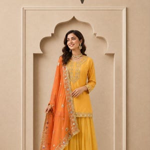 May include: A yellow three-piece outfit consisting of a long-sleeved tunic with gold embroidery, a matching pleated skirt, and an orange sheer dupatta featuring gold borders and small mirror embellishments. The text EV Ethnic Villa is visible.