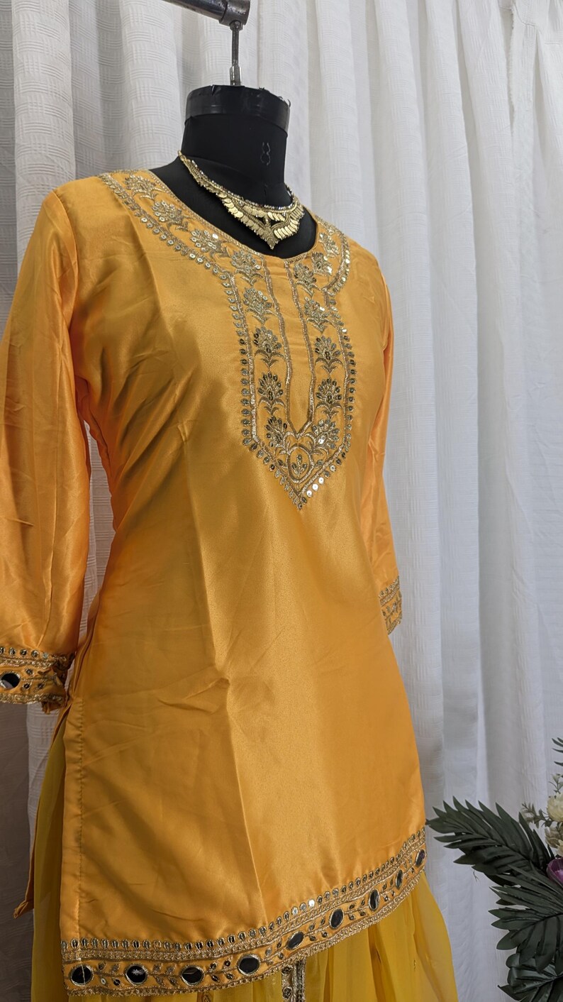 May include: A bright yellow tunic featuring three-quarter sleeves and a round neckline. The garment is adorned with intricate gold embroidery and reflective mirror embellishments along the neckline, sleeve cuffs, and the lower hemline.
