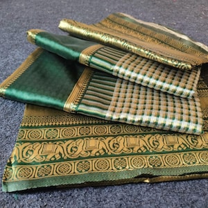May include: Folded green and gold fabric with intricate patterns. The fabric features a gold border with elephant motifs and a checkered pattern in white, green, and gold. The fabric is layered on a grey surface.
