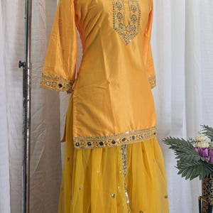 May include: A bright yellow tunic and skirt set featuring gold embroidery and small circular mirrors. The tunic has three-quarter sleeves and a decorative neckline, while the sheer yellow skirt is adorned with scattered metallic sequins.