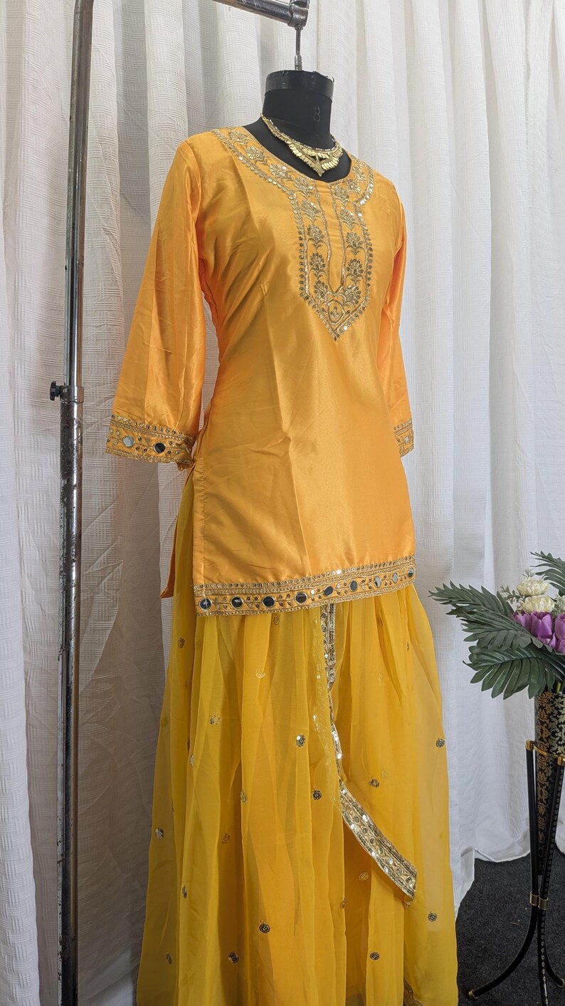 May include: A bright yellow tunic and skirt set featuring gold embroidery and small circular mirrors. The tunic has three-quarter sleeves and a decorative neckline, while the sheer yellow skirt is adorned with scattered metallic sequins.