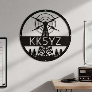 Peut inclure: Décoration murale en métal noir représentant une tour de radio dans un cercle. Le design comprend des éclairs, une tour et les lettres "KK5YZ". Une silhouette de forêt est en bas du cercle.