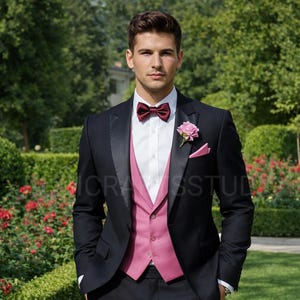 May include: A black suit with a satin lapel, worn with a white shirt, a pink waistcoat, and a matching bow tie and pocket square. A pink rose is pinned to the lapel. The suit is worn outdoors in a garden setting.