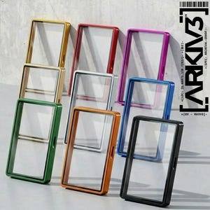 Puede incluir: Una colección de vitrinas rectangulares en varios colores, incluyendo dorado, rojo, morado, azul y negro. Cada vitrina tiene un centro transparente. Las vitrinas están dispuestas en diferentes ángulos. El texto "ARKIV3" es visible.