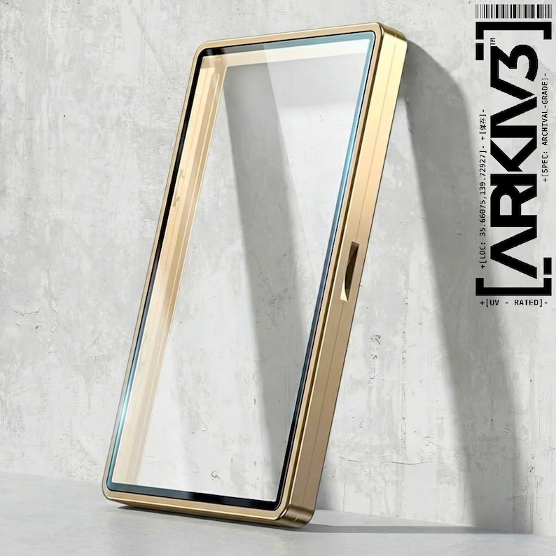 May include: A gold-colored rectangular phone case with a clear glass screen protector. The case is leaning against a textured gray wall. The text "ARKIV3" and other details are printed on the right side of the image.