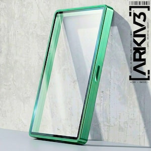 May include: A rectangular, green-framed object with a clear, transparent center, leaning against a textured, light gray wall. The frame has a metallic sheen. The text "ARKIV3" and other technical details are printed on the right side.
