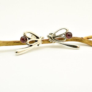 May include: A pair of silver dragonfly earrings with red gemstone accents.