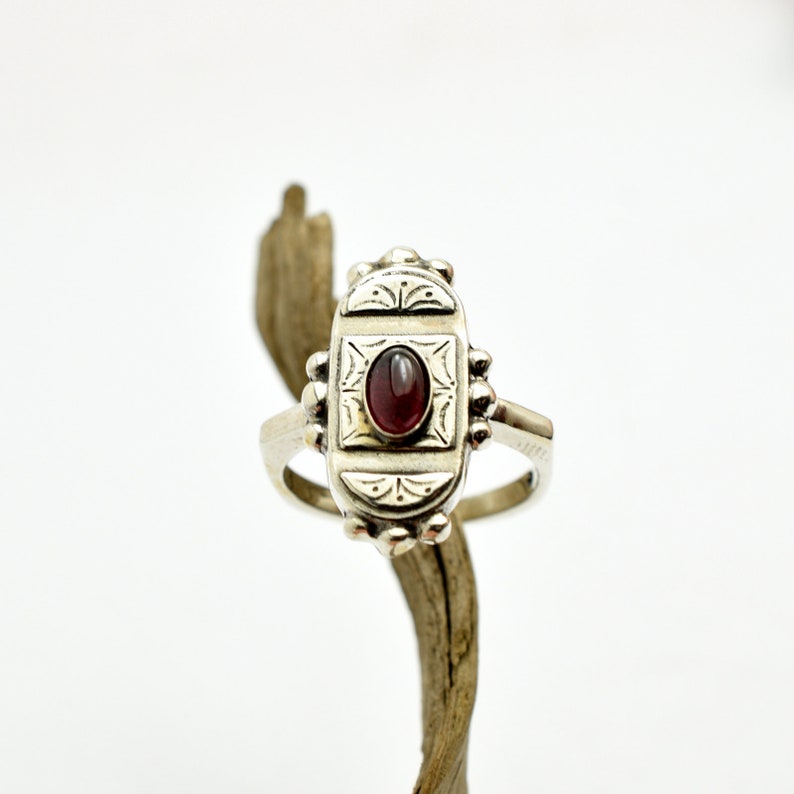 Pu&ograve; includere: Un anello d'argento con un designo ornato e una pietra preziosa rossa al centro.