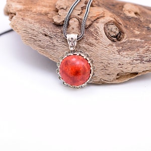 May include: A silver chain necklace with a red coral pendant. The pendant is round and has a silver bezel setting.