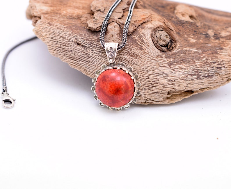 May include: A silver chain necklace with a red coral pendant. The pendant is round and has a silver bezel setting.
