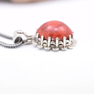 May include: A silver necklace with a red coral pendant. The pendant is set in a silver bezel with a decorative border.