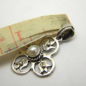 May include: Silver pendant featuring a white pearl at its centre and a floral design. The pendant has a loop at the top for attaching to a chain.