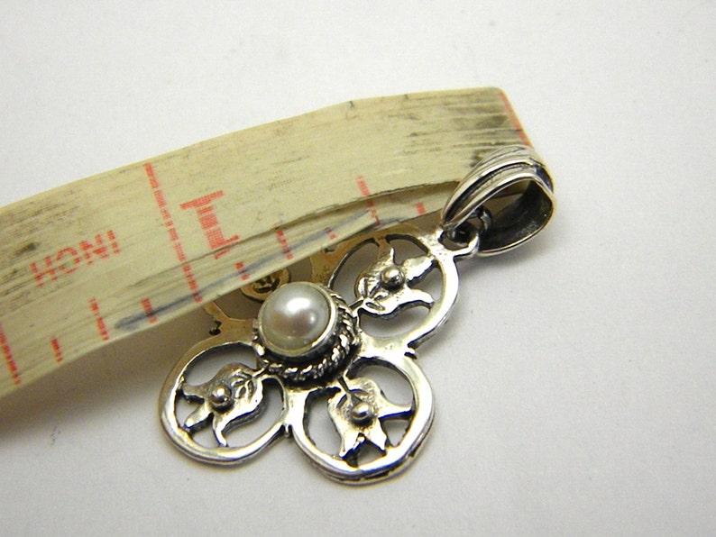 May include: Silver pendant featuring a white pearl at its centre and a floral design. The pendant has a loop at the top for attaching to a chain.