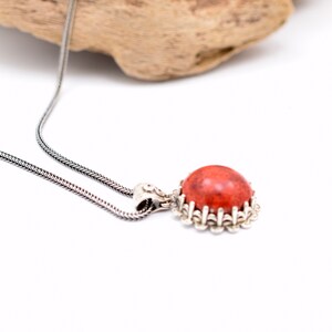 May include: A silver chain necklace with a pendant featuring a round, red coral stone set in a silver filigree frame.