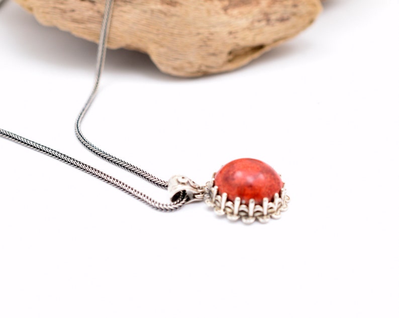 May include: A silver chain necklace with a pendant featuring a round, red coral stone set in a silver filigree frame.