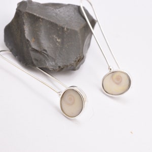May include: A pair of silver dangle earrings with a white shell inlay. The shell has a spiral pattern.