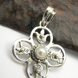May include: A silver pendant with a delicate, intricate design featuring four stylised flowers surrounding a white pearl in the centre. The pendant has a loop at the top for attaching to a chain.