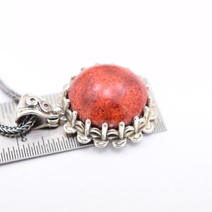 May include: A silver necklace with a red coral pendant. The pendant is set in a silver frame with a decorative design.
