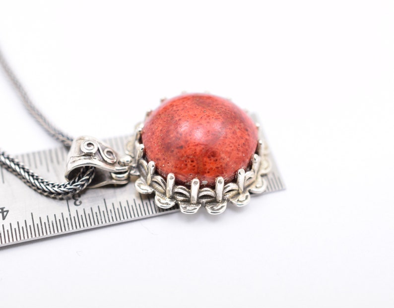 May include: A silver necklace with a red coral pendant. The pendant is set in a silver frame with a decorative design.
