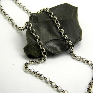 Può includere: Una collana a catena d'argento con un motivo a maglie rotonde. La catena è appoggiata su una roccia grigio scuro.