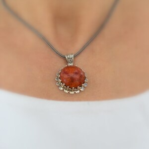 May include: A silver chain necklace with a round pendant featuring a red coral stone set in a silver filigree frame.