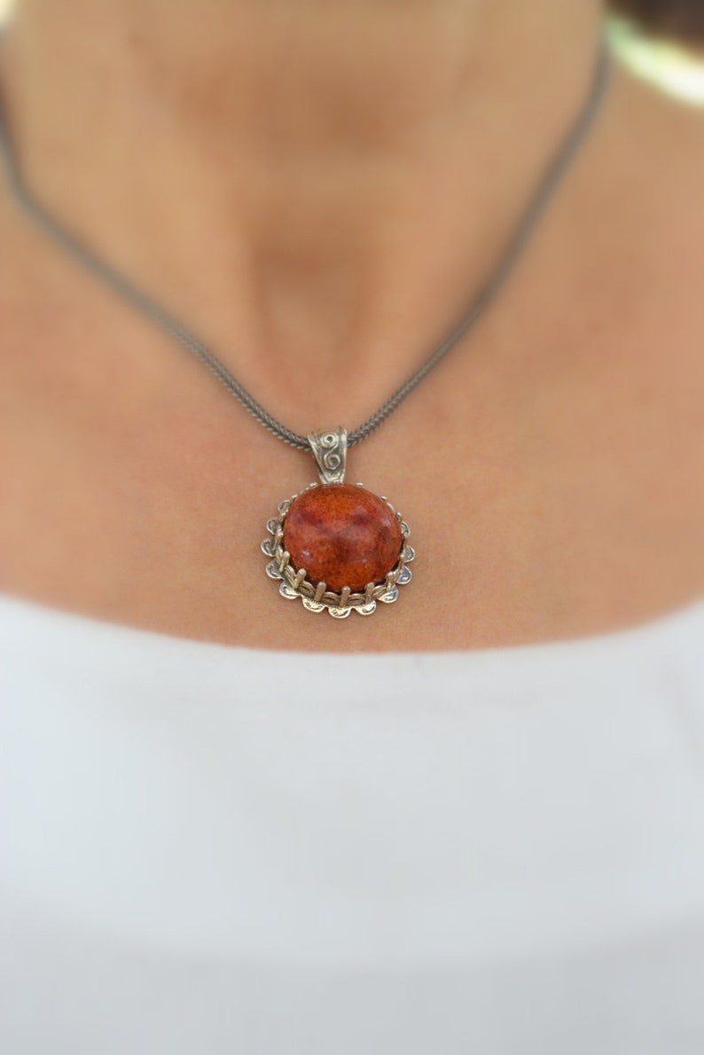 May include: A silver chain necklace with a round pendant featuring a red coral stone set in a silver filigree frame.