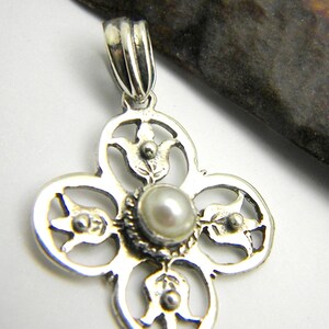 May include: A silver pendant with a delicate, intricate design featuring four circular shapes with floral motifs. A small, white pearl is set in the centre of the pendant.