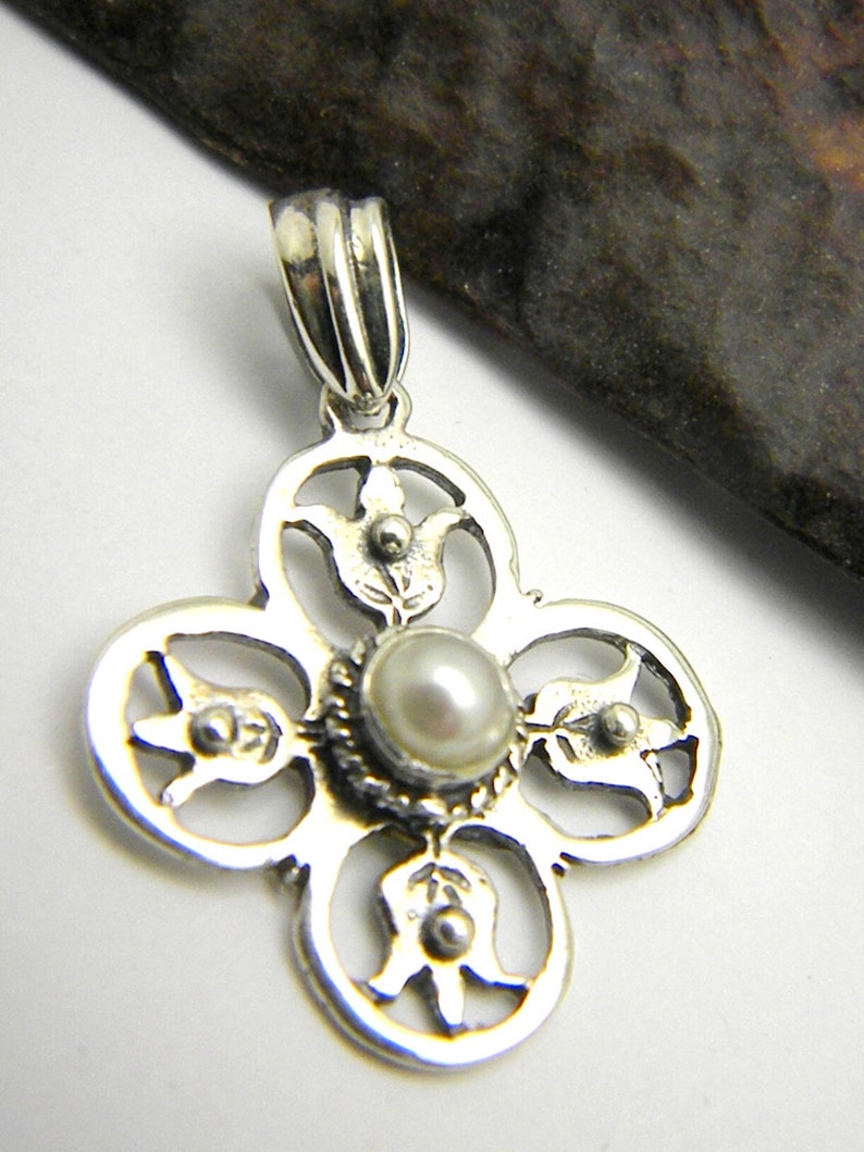 May include: A silver pendant with a delicate, intricate design featuring four circular shapes with floral motifs. A small, white pearl is set in the centre of the pendant.