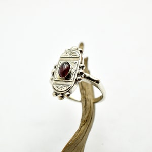 Pu&ograve; includere: Un anello d'argento con una montatura ovale che presenta una pietra preziosa rossa e dettagli incisi intricati.