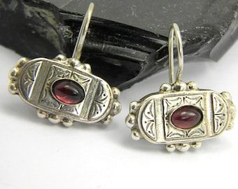 May include: A pair of silver earrings with a red gemstone set in a decorative frame.