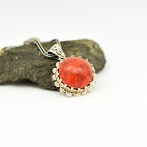 May include: A silver pendant necklace with a red coral stone set in a silver filigree frame.