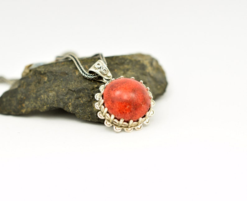 May include: A silver pendant necklace with a red coral stone set in a silver filigree frame.
