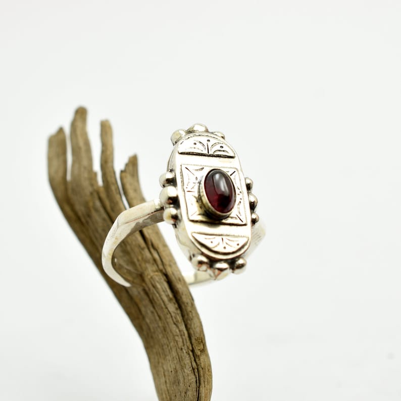 Pu&ograve; includere: Un anello d'argento con una montatura ovale che presenta una pietra rossa e dettagli incisi intricati.