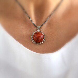 May include: A silver chain necklace with a round pendant featuring a red coral stone set in a silver bezel.