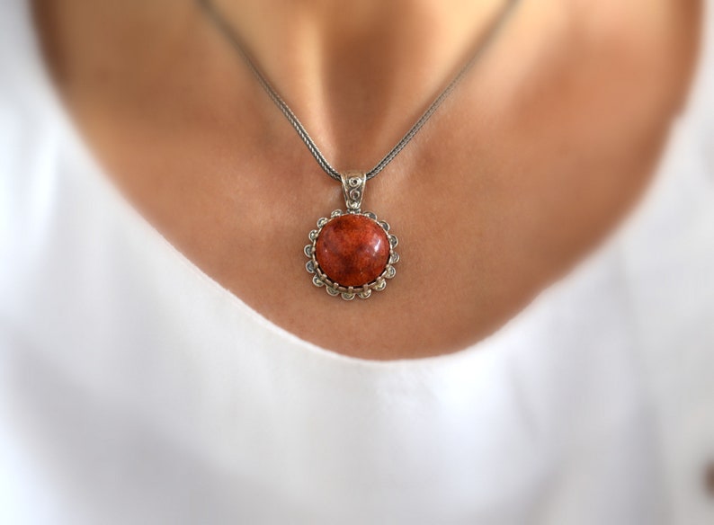 May include: A silver chain necklace with a round pendant featuring a red coral stone set in a silver bezel.